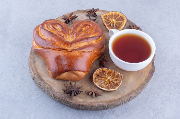 Anís estrellado rodajas de limón secas, una taza de té y un bollo dulce sobre una tabla de madera sobre superficie de mármol