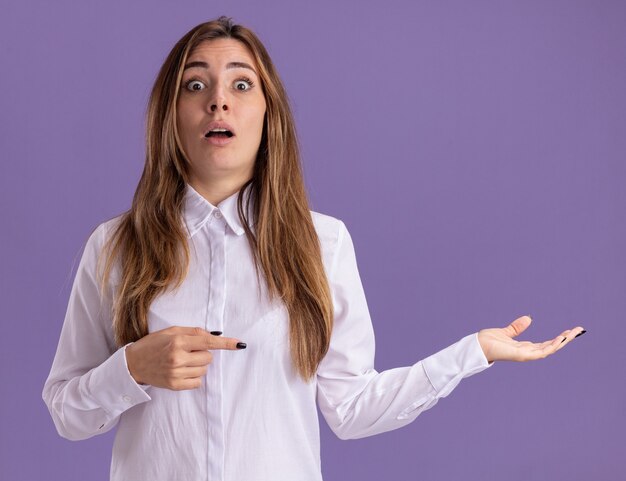 Ansiosa joven bastante caucásica apunta a la mano vacía en púrpura