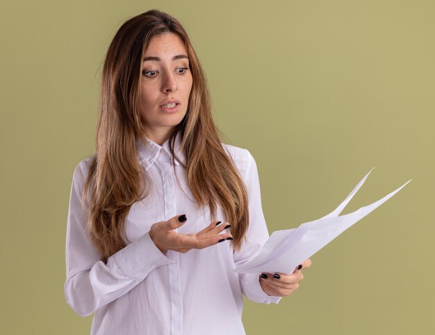 Ansiosa joven bastante caucásica sostiene y mira hojas de papel en blanco