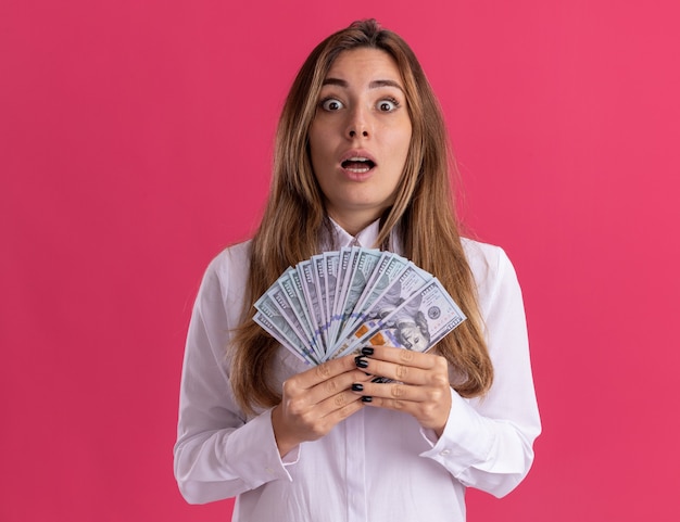 Ansiosa joven bastante caucásica tiene dinero aislado en la pared rosa con espacio de copia