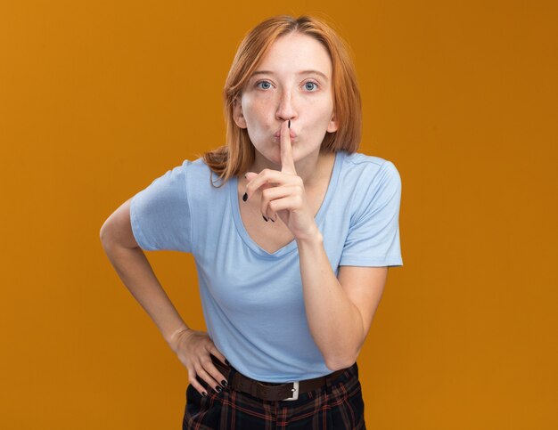 Ansiosa joven pelirroja pelirroja con pecas haciendo gesto de silencio en naranja