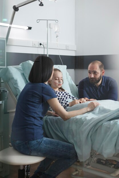 Ansiosa pareja estresada discutiendo sobre la evolución de la enfermedad de la niña mientras se encuentra en la sala de recuperación de pacientes del hospital pediátrico. Padres jóvenes nerviosos preocupados hablando sobre el tratamiento de la salud.