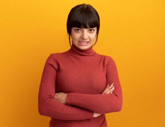 Ansioso joven morena caucásica se encuentra con los brazos cruzados aislado en la pared naranja con espacio de copia