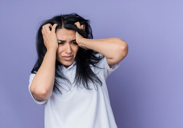 Ansioso joven morena caucásica sostiene la cabeza mirando al lado aislado en la pared púrpura