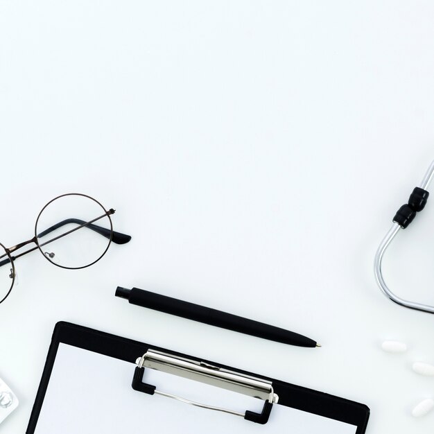 Los anteojos; bolígrafo; portapapeles; pastillas y un estetoscopio sobre fondo blanco