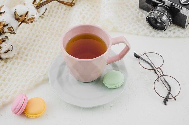 Los anteojos; cámara; ramita de algodón con taza de té de hierbas y macarrones sobre fondo blanco