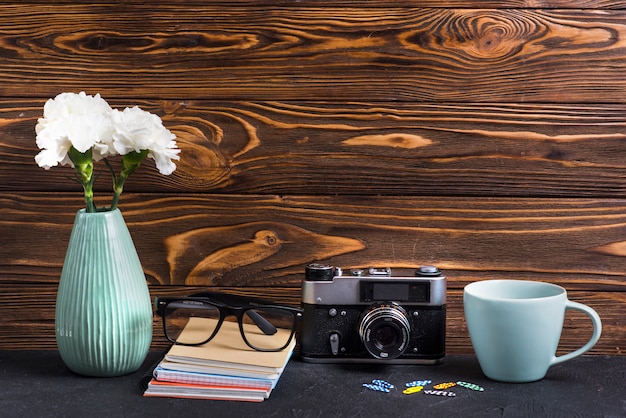 Foto gratuita los anteojos; libros; clip de papel; copa y cámara vintage contra fondo texturado de madera