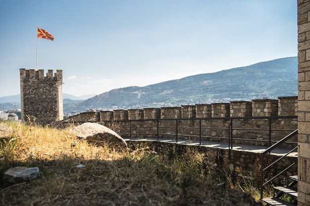 Antiguo castillo con la bandera de Macedonia rodeado de colinas cubiertas de vegetación