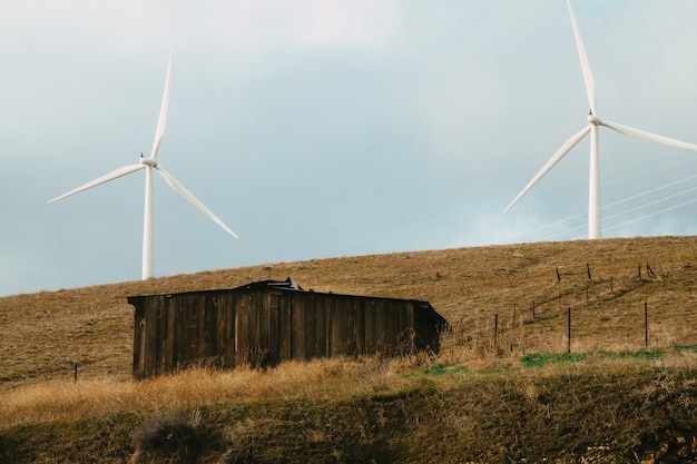 Antiguo granero de madera en un campo con dos molinos de viento bajo la luz del sol durante el día