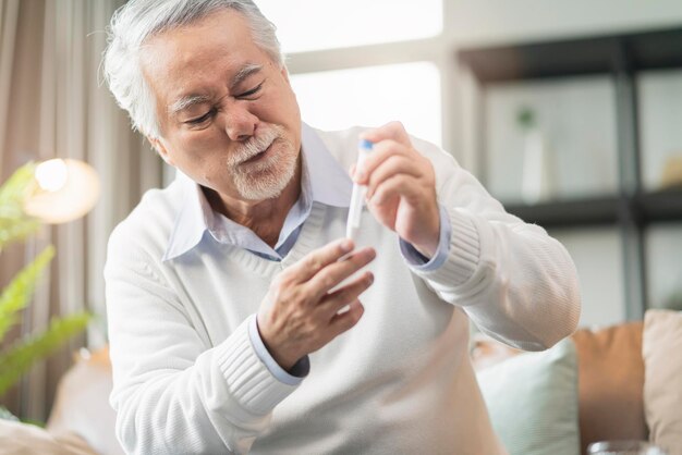Antiguo hisopo nasal masculino asiático senior que prueba pruebas rápidas por sí mismo para la detección del virus SARS co2 en el hogar aislar el concepto de cuarentena