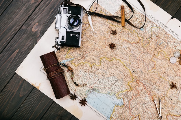 Antiguo mapa amarillo, gafas, monedas, estuche de cuero, cámara, reloj, brújulas, granos de café, otras especias y galletas se encuentran en el piso de madera