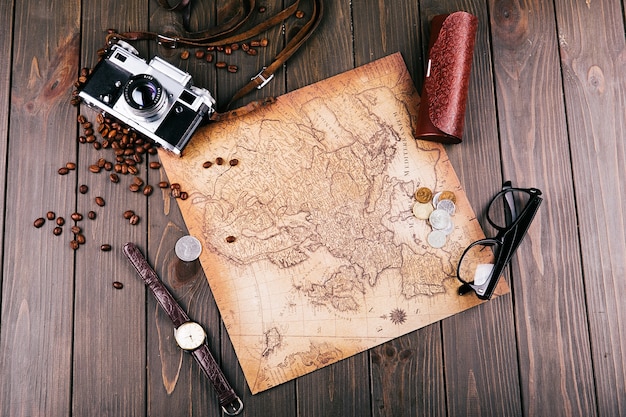 Antiguo mapa amarillo, gafas, monedas, estuche de cuero, cámara, reloj, granos de café y otras especias se encuentran en piso de madera