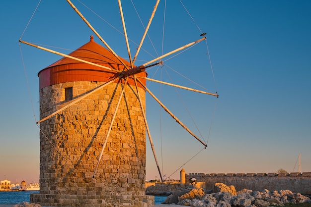 Antiguo molino de viento en la bahía durante la puesta de sol en la ciudad de Rodas en la isla de Rodas de la isla del archipiélago del Dodecaneso vacaciones en Europa y un popular destino turístico