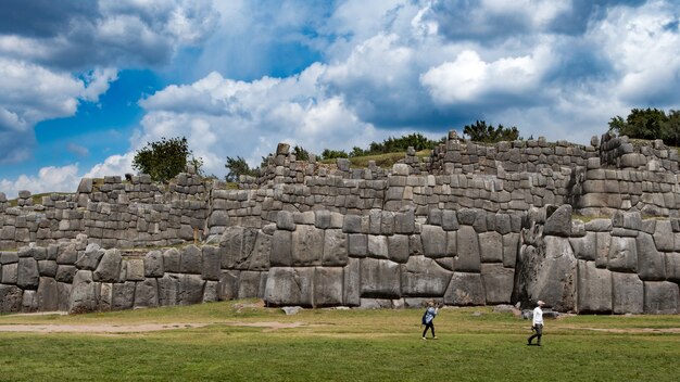 Antiguo muro de piedra y turistas cerca de él con un cielo azul
