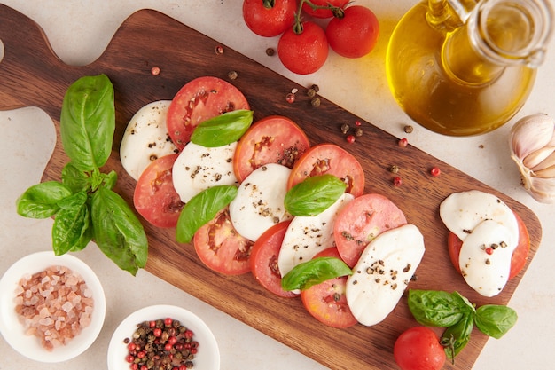 Antipasto de ensalada italiana fresca llamado caprese con mozzarella de búfala, tomates en rodajas y albahaca con aceite de oliva. Ingredientes para ensalada caprese vegetariana. Comida italiana. vista superior. Estilo rústico.