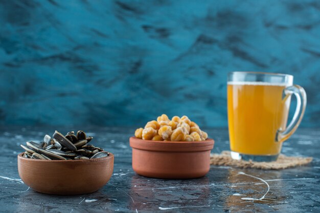 Aperitivos en cuencos junto a un vaso de cerveza en textura, sobre fondo azul.