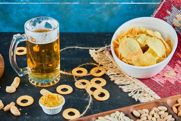 Aperitivos variados, patatas fritas y un vaso de cerveza en la mesa oscura.
