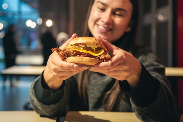 Foto gratuita una apetitosa hamburguesa de pollo en manos femeninas en un restaurante de comida rápida