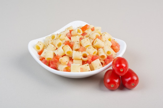 Apetitosa pasta penne con especias y rodajas de tomate en la placa blanca.