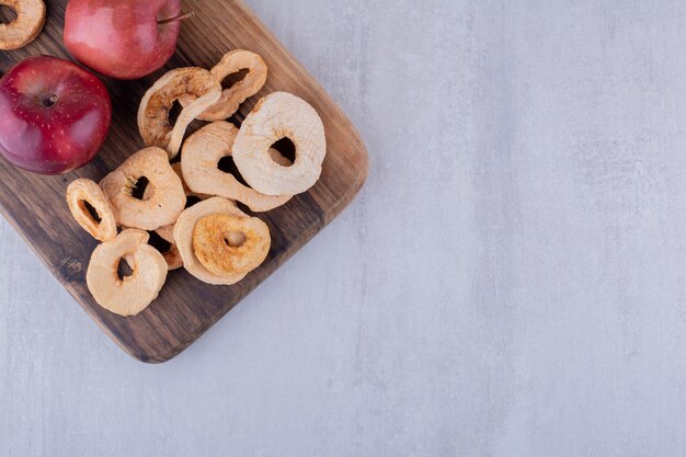 Apetitosas rodajas de manzana seca y manzanas enteras sobre una tabla de madera sobre fondo blanco.