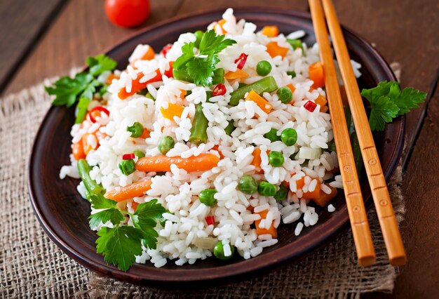 Apetitoso arroz saludable con verduras en plato blanco sobre una mesa de madera.