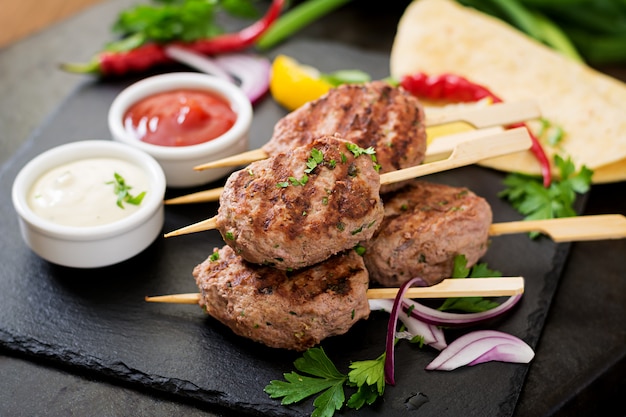 Apetitoso kofta kebab (albóndigas) con salsa y tacos de tortillas en mesa negra