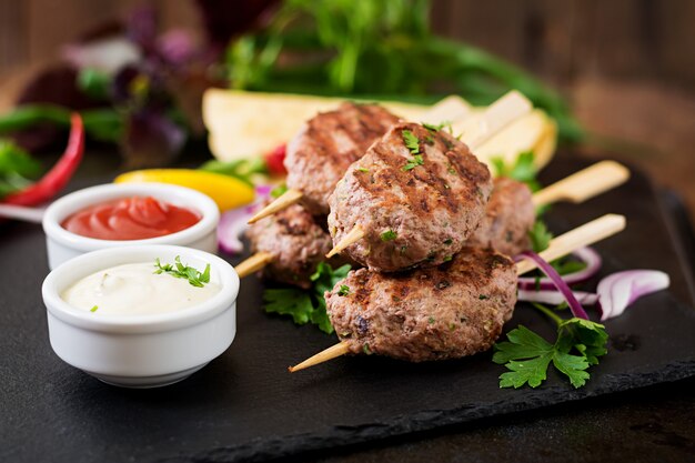 Apetitoso kofta kebab (albóndigas) con salsa y tacos de tortillas en mesa negra