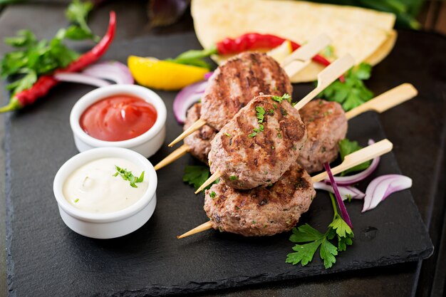 Apetitoso kofta kebab (albóndigas) con salsa y tacos de tortillas en mesa negra