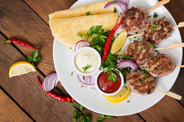 Apetitoso kofta kebab (albóndigas) con salsa y tacos de tortillas en un plato blanco