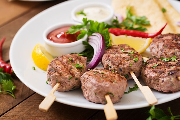 Apetitoso kofta kebab (albóndigas) con salsa y tacos de tortillas en un plato blanco