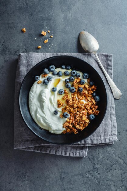 Apetitoso muesli casero con bayas y yogur servido en un tazón sobre fondo oscuro.