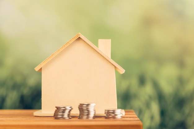 Apilado de monedas cerca de la casa de madera en la mesa al aire libre