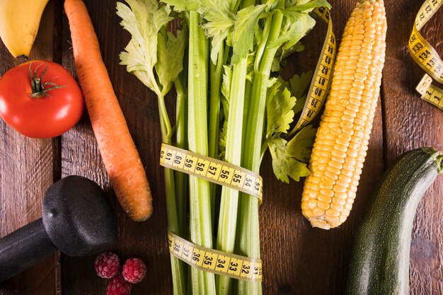 Apio envuelto con cinta métrica cerca de verduras y pesas