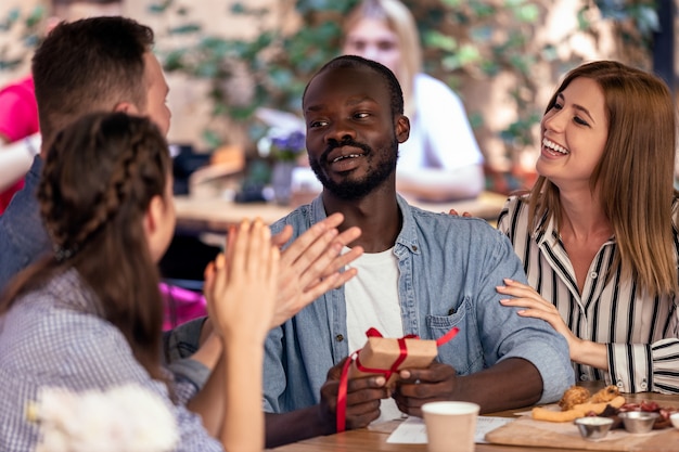 Aplausos y regalos para un niño africano de sus amigos caucásicos en el acogedor café