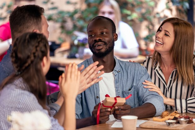 Aplausos y regalos para un niño africano de sus amigos caucásicos en el acogedor café