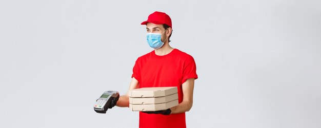 Aplicación de entrega de alimentos compras en línea sin contacto y concepto covid19 Repartidor agradable con guantes de uniforme rojo y mascarilla que da orden al cliente con terminal POS entrega pizza