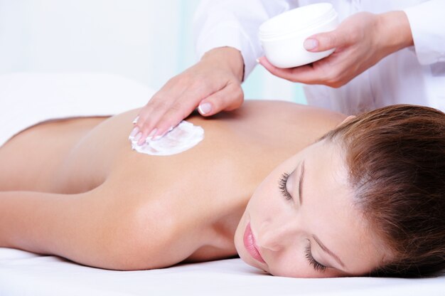 Aplicar crema hidratante en la espalda femenina antes del masaje
