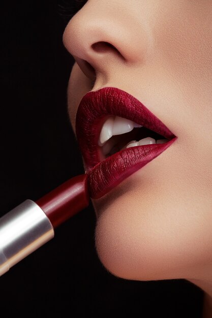 Aplicar lápiz labial rojo en los labios en una foto de cerca sobre fondo negro. Belleza y maquillaje