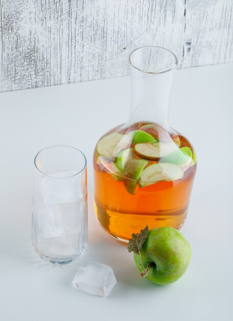 Apple con bebida, cubitos de hielo en vidrio en blanco y sucio, vista de ángulo alto.