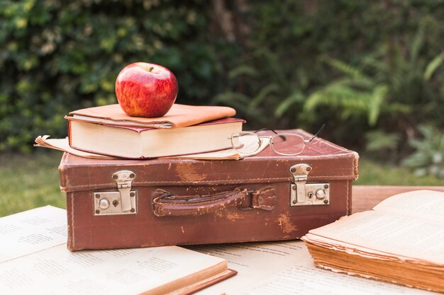 Apple y gafas acostado en la maleta cerca de libros