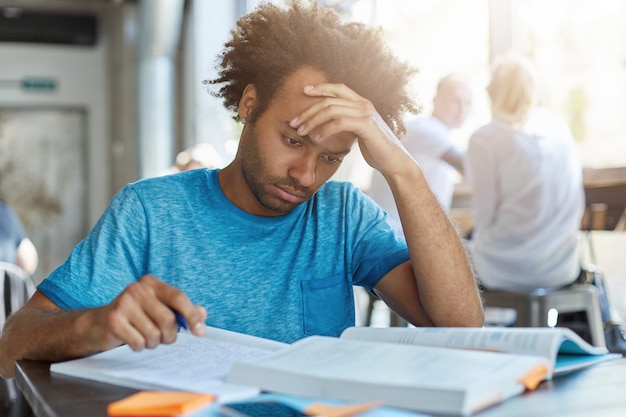 Aprendizaje y educación. Retrato interior de un graduado de secundaria afroamericano concentrado y trabajador que se prepara para los exámenes de admisión a la universidad y la prueba de inscripción, escribiendo notas del libro de texto