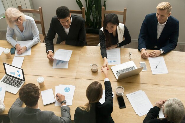 Apretón de manos de las empresarias asiáticas y caucásicas en la reunión de grupo, visión superior