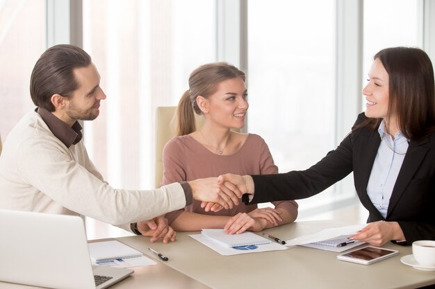 Apretón de manos del hombre de negocios y de la empresaria en la reunión de negocios que se sienta en oficina