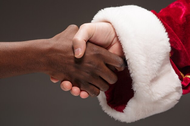 El apretón de manos de la mano de Santa Claus y la mano del hombre africano. Concepto de feliz navidad