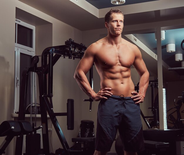 Un apuesto culturista musculoso sin camisa posando en el gimnasio.