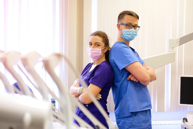 Un apuesto dentista masculino con una asistente femenina, de pie en una oficina de dentista.
