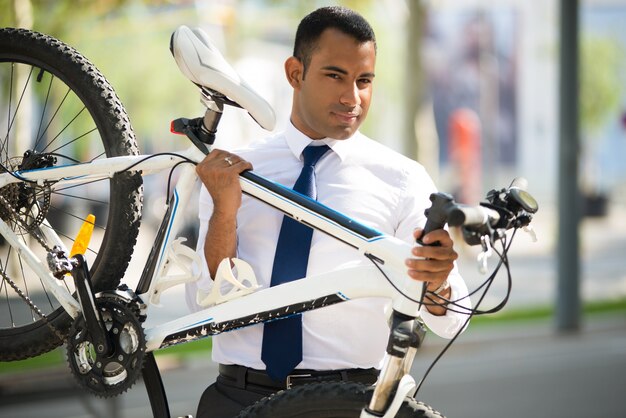 Apuesto empleado de oficina llevando su bicicleta roto