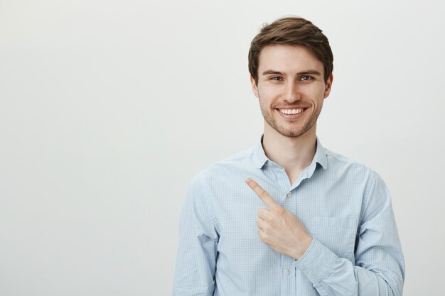 Apuesto empresario masculino exitoso que señala el dedo en la esquina superior izquierda, sonriendo