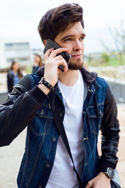 Apuesto estudiante usando teléfono móvil en la calle.