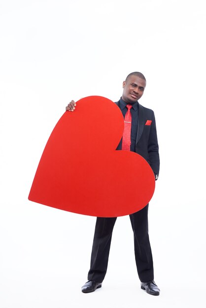 Apuesto hombre africano vistiendo en suite negro y corbata roja con gran corazón rojo